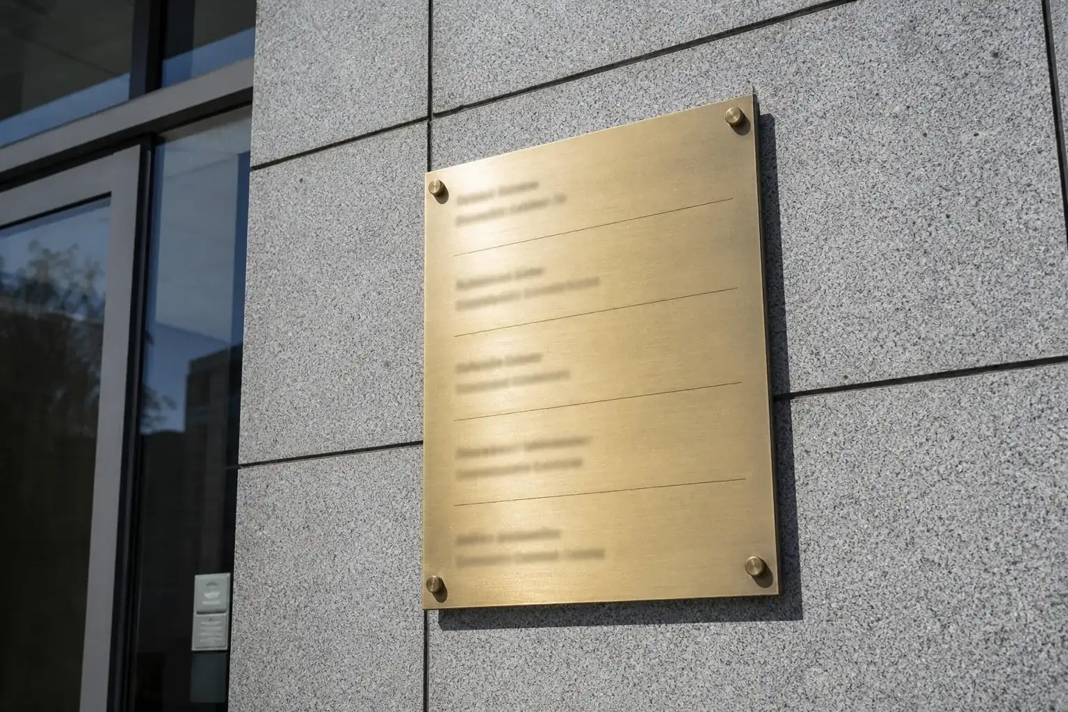 Plaque professionnelle en laiton sur la façade d’un immeuble de bureaux en granit breton, plusieurs sociétés domiciliées